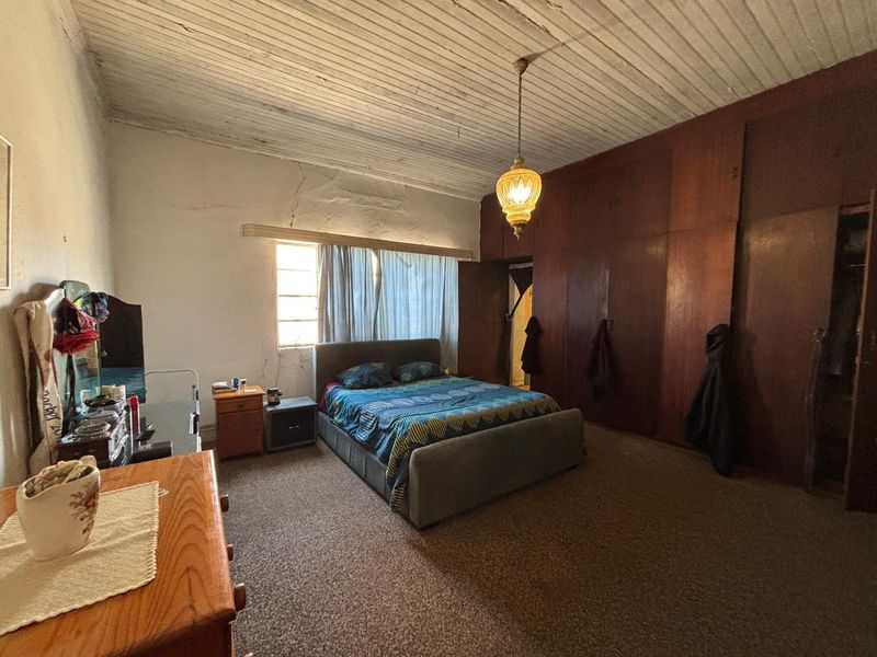 Spacious bedroom featuring extensive built-in wooden cabinetry, a unique timber plank ceiling, and carpeted flooring, requiring some cosmetic updates to the walls and ceiling.