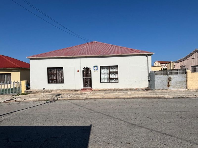 Front elevation of a single-story house featuring a corrugated metal roof, security-barred windows, and a metal driveway gate.