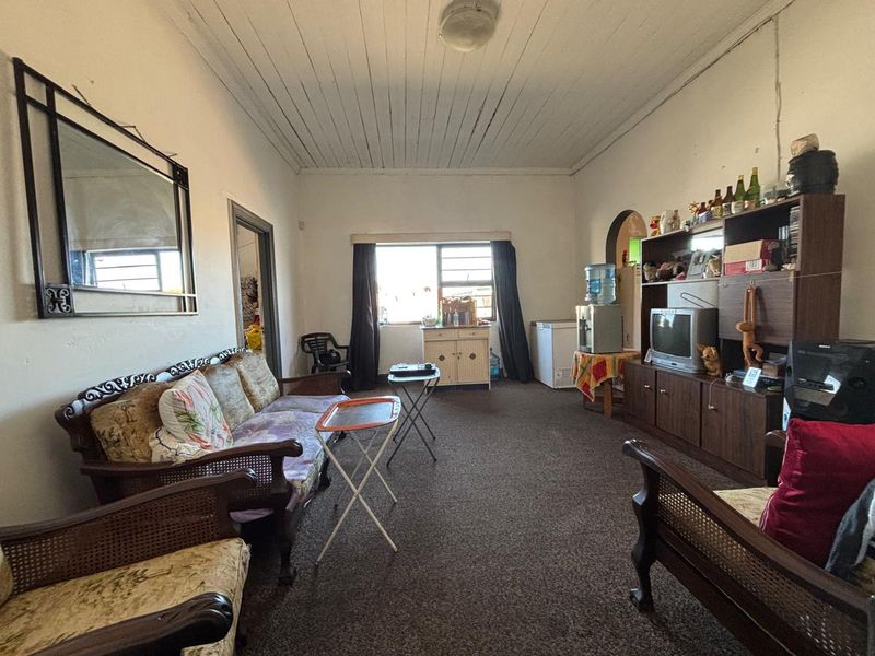 A living room featuring a timber-paneled ceiling and a sliding window, currently showing signs of wear in the flooring and wall finishes.