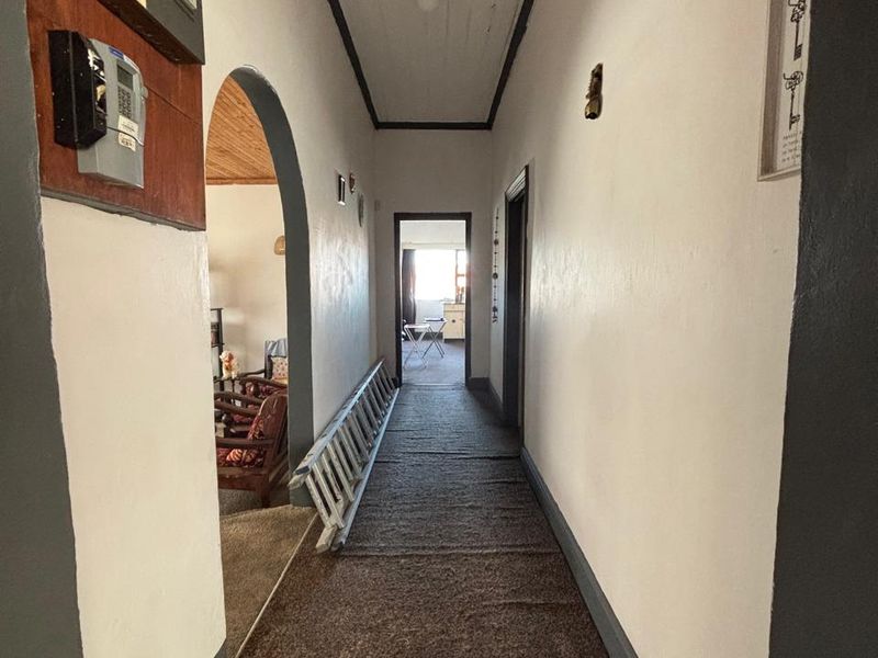 A long interior hallway featuring an arched entryway, timber ceiling, and carpeted flooring, providing access to multiple rooms within the home.