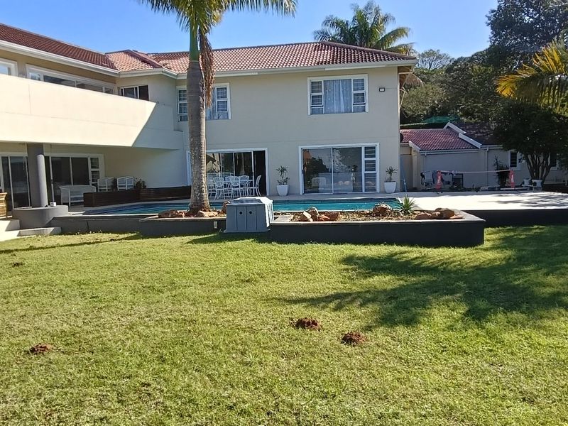 Rear view of the townhouse featuring a swimming pool, paved patio area, and a spacious landscaped garden with mature palm trees.