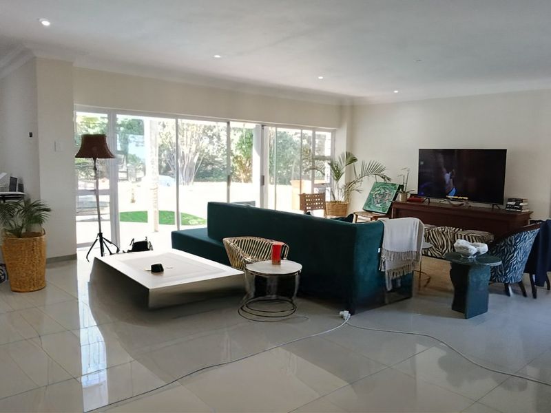 Spacious open-plan living area featuring large sliding glass doors, polished porcelain floor tiles, and recessed downlighting, offering a bright and modern atmosphere.