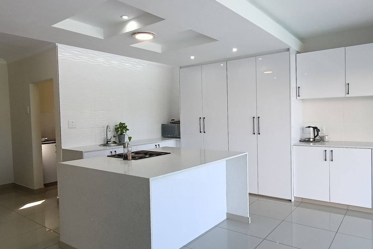 Modern kitchen featuring a central island with a gas cooktop, sleek white cabinetry, and polished tiled flooring.