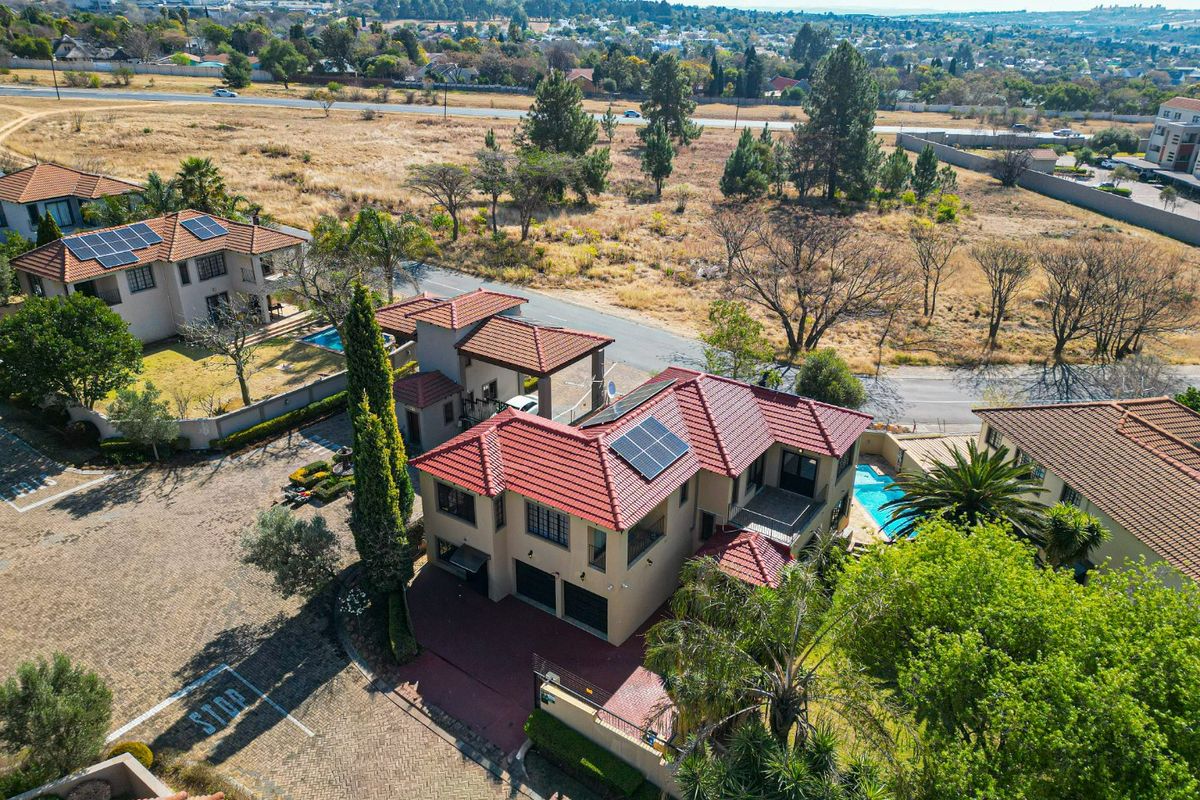 Aerial view of a residential property featuring a tiled roof with solar panels, a private swimming pool, and a paved driveway.