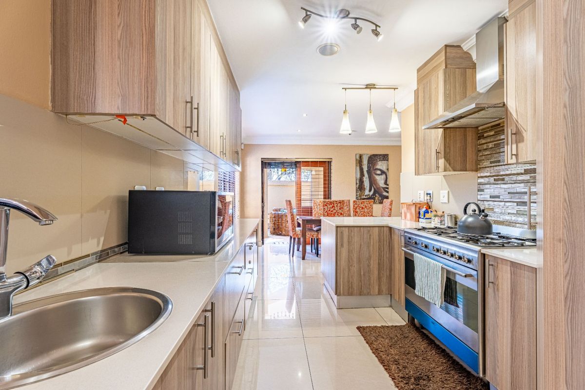 Modern kitchen featuring wood-finish cabinetry, stone countertops, a gas stove with extractor fan, and a mosaic tile backsplash, leading into an open-plan dining area.