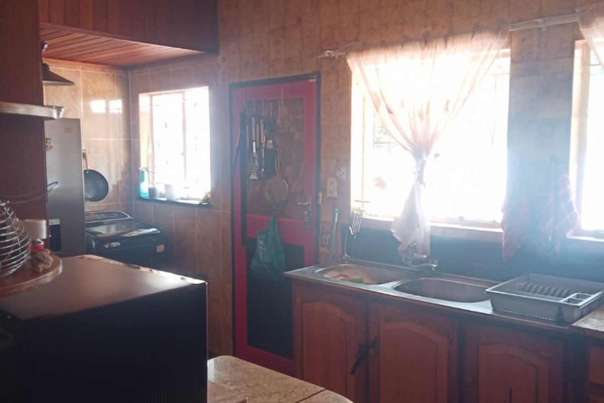 A dated kitchen featuring traditional wooden cabinetry, stone countertops, and a double basin sink, offering potential for a modern renovation.