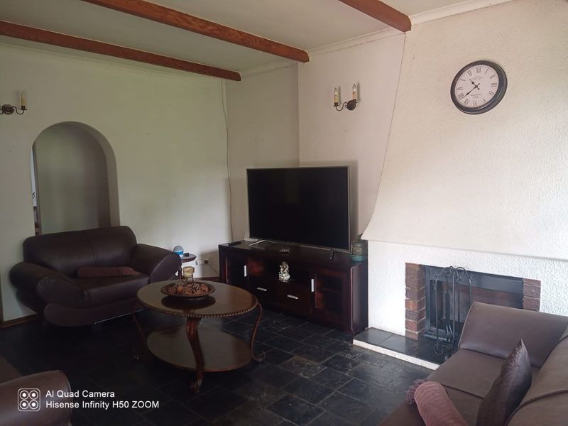 Living room featuring a traditional fireplace with a brick hearth, exposed timber ceiling beams, and dark stone tile flooring.