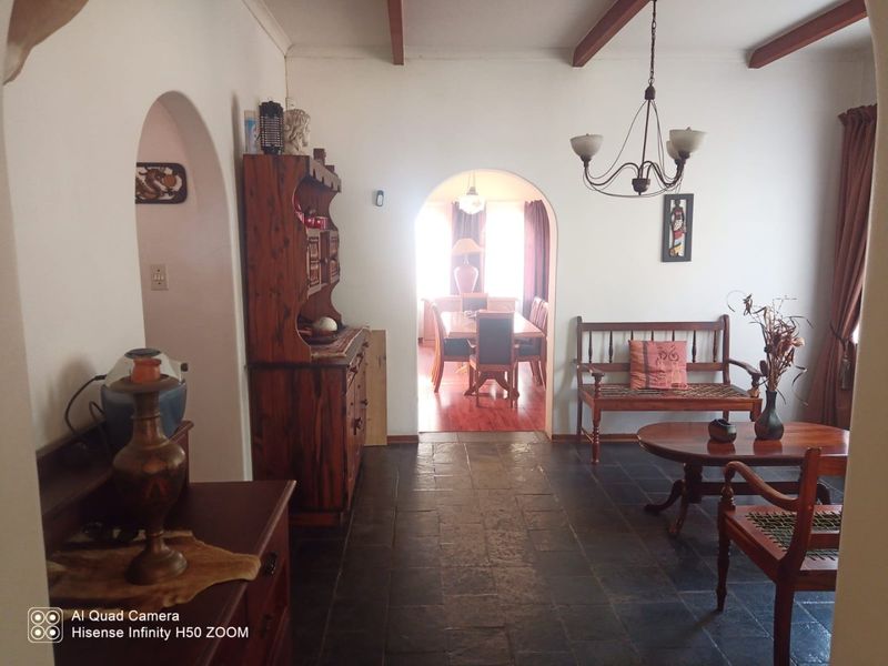 A living room featuring stone tile flooring, exposed timber ceiling beams, and arched architectural transitions leading to an adjacent dining area.
