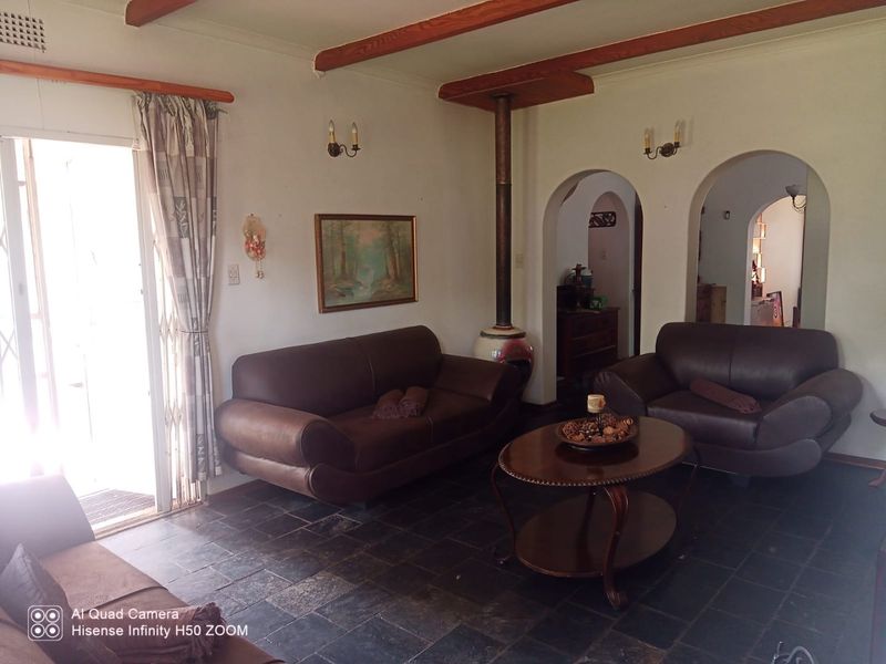 Living room featuring slate tile flooring, exposed timber ceiling beams, a freestanding fireplace, and arched doorways leading to adjacent spaces.