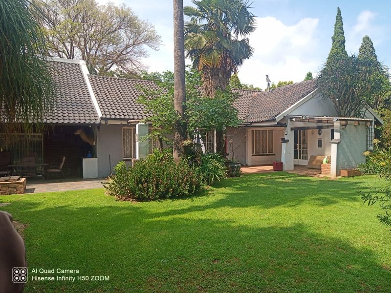 Rear view of the house featuring a covered patio area, established garden, and tiled roof structure.