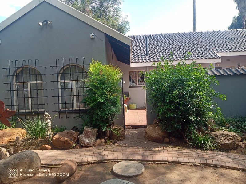 Rear exterior view of the house featuring a paved walkway, landscaped garden area, and security bars on the windows.