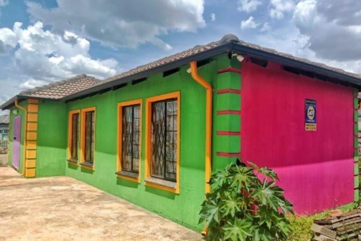 Rear view of a detached house featuring a tiled roof, security bars on windows, and exterior walls with a vibrant, non-standard paint scheme.