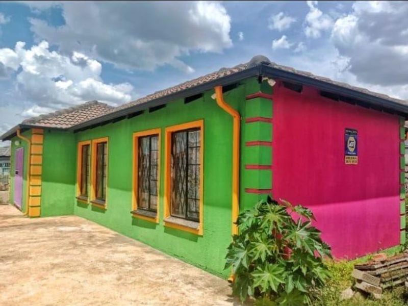 Rear view of a detached house featuring a tiled roof, security bars on windows, and exterior walls with a vibrant, non-standard paint scheme.