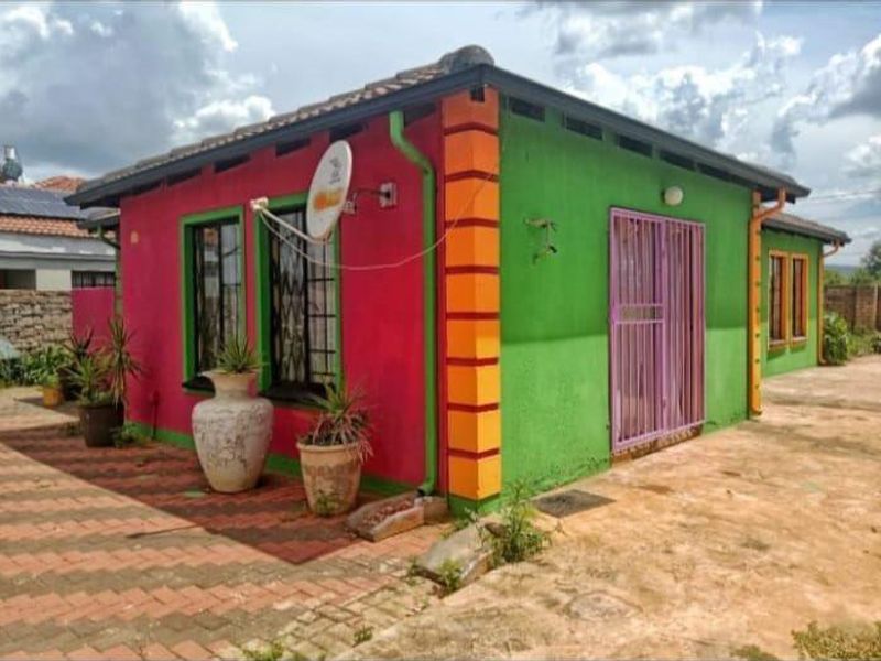 Rear view of a detached house featuring a vibrant multi-colored exterior facade, security gates, and paved surrounding area.