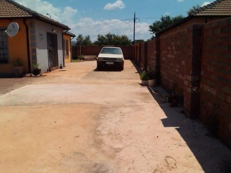 A view of the property's front exterior, featuring a concrete driveway, brick boundary wall, and tiled roof structure.