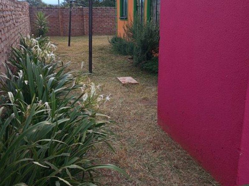 A rear garden area featuring a brick boundary wall, paved walkway, and metal washing line poles alongside the exterior wall of the house.