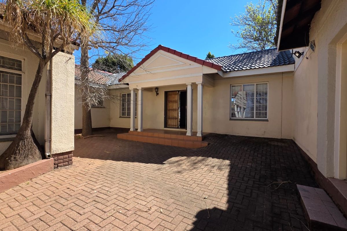 A paved rear courtyard featuring a covered entrance porch with decorative columns and classic tiled roof architecture.