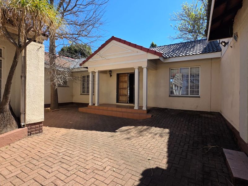 A paved rear courtyard featuring a covered entrance porch with decorative columns and classic tiled roof architecture.