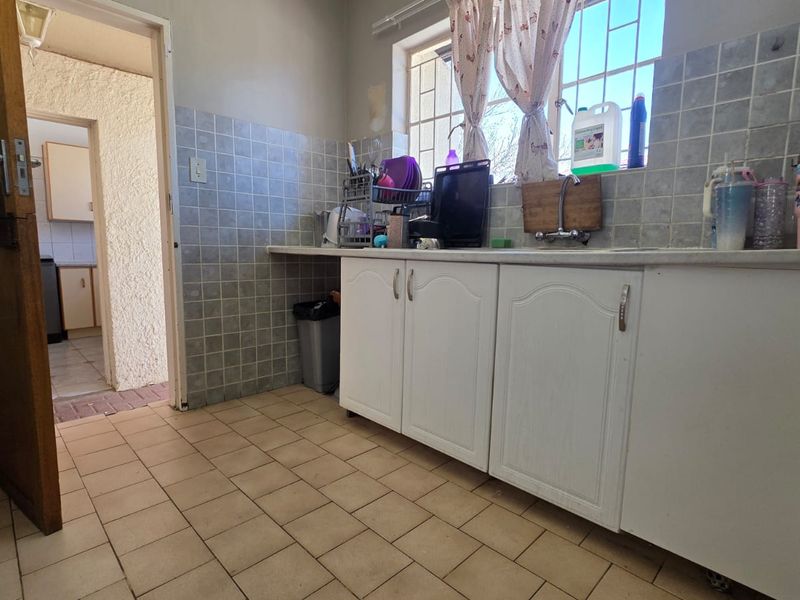 A functional scullery area featuring tiled flooring, a built-in sink, and tiled splashbacks, providing a practical space for food preparation and cleaning.