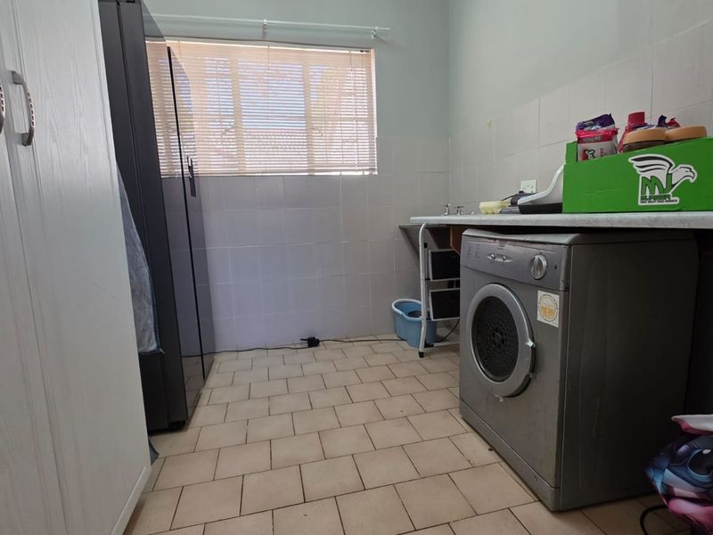 A functional laundry room featuring tiled flooring, a tiled splashback, and built-in cabinetry with space for laundry appliances.