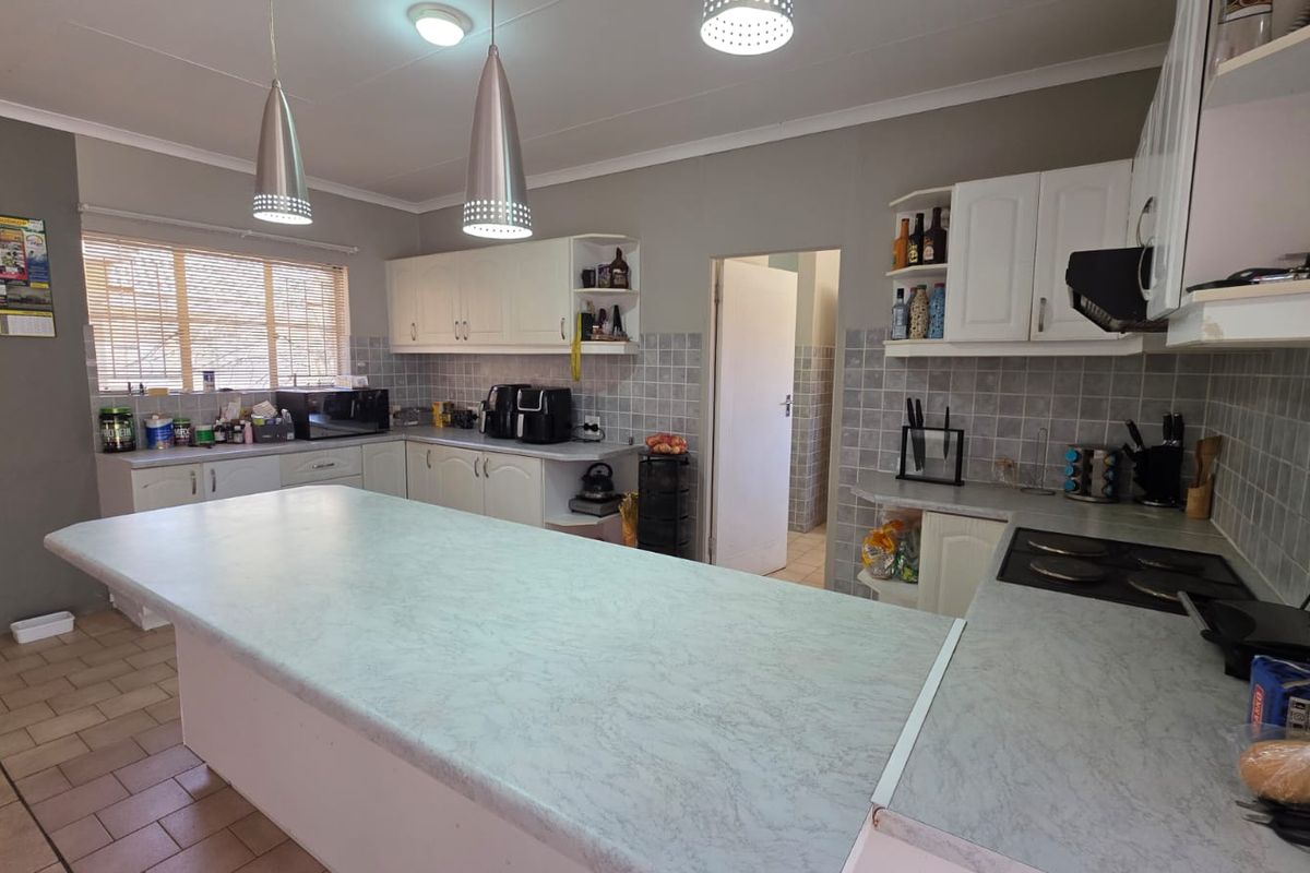 A functional kitchen featuring a central island, ample built-in cabinetry, tiled backsplash, and an integrated electric hob with pendant lighting.