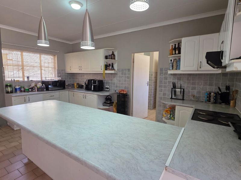 A functional kitchen featuring a central island, ample built-in cabinetry, tiled backsplash, and an integrated electric hob with pendant lighting.