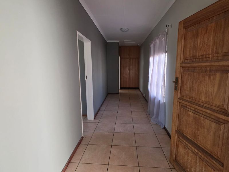 A clean, well-lit hallway featuring neutral wall tones, tiled flooring, and built-in storage cupboards at the end of the passage.