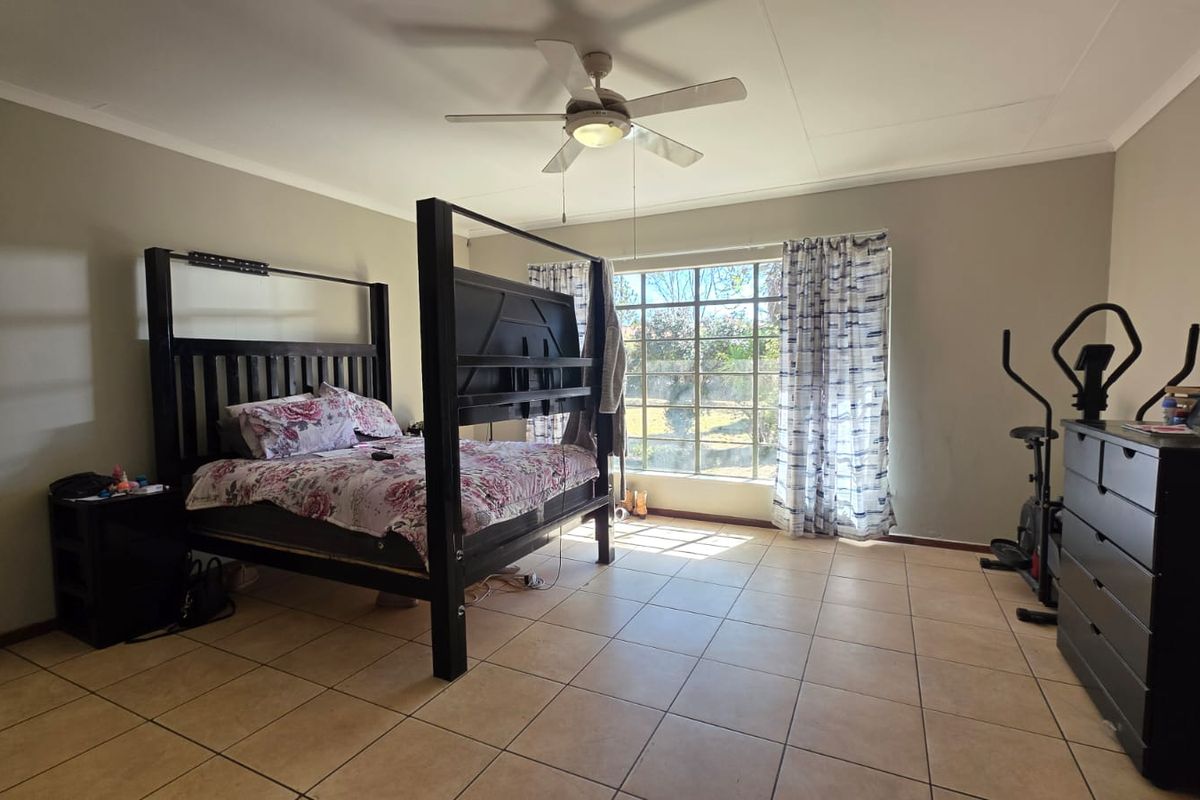 Spacious bedroom featuring neutral wall tones, tiled flooring, and a ceiling fan, providing a comfortable and functional living space.