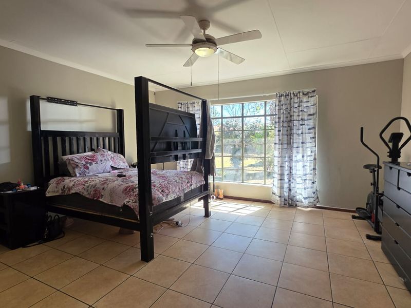 Spacious bedroom featuring neutral wall tones, tiled flooring, and a ceiling fan, providing a comfortable and functional living space.