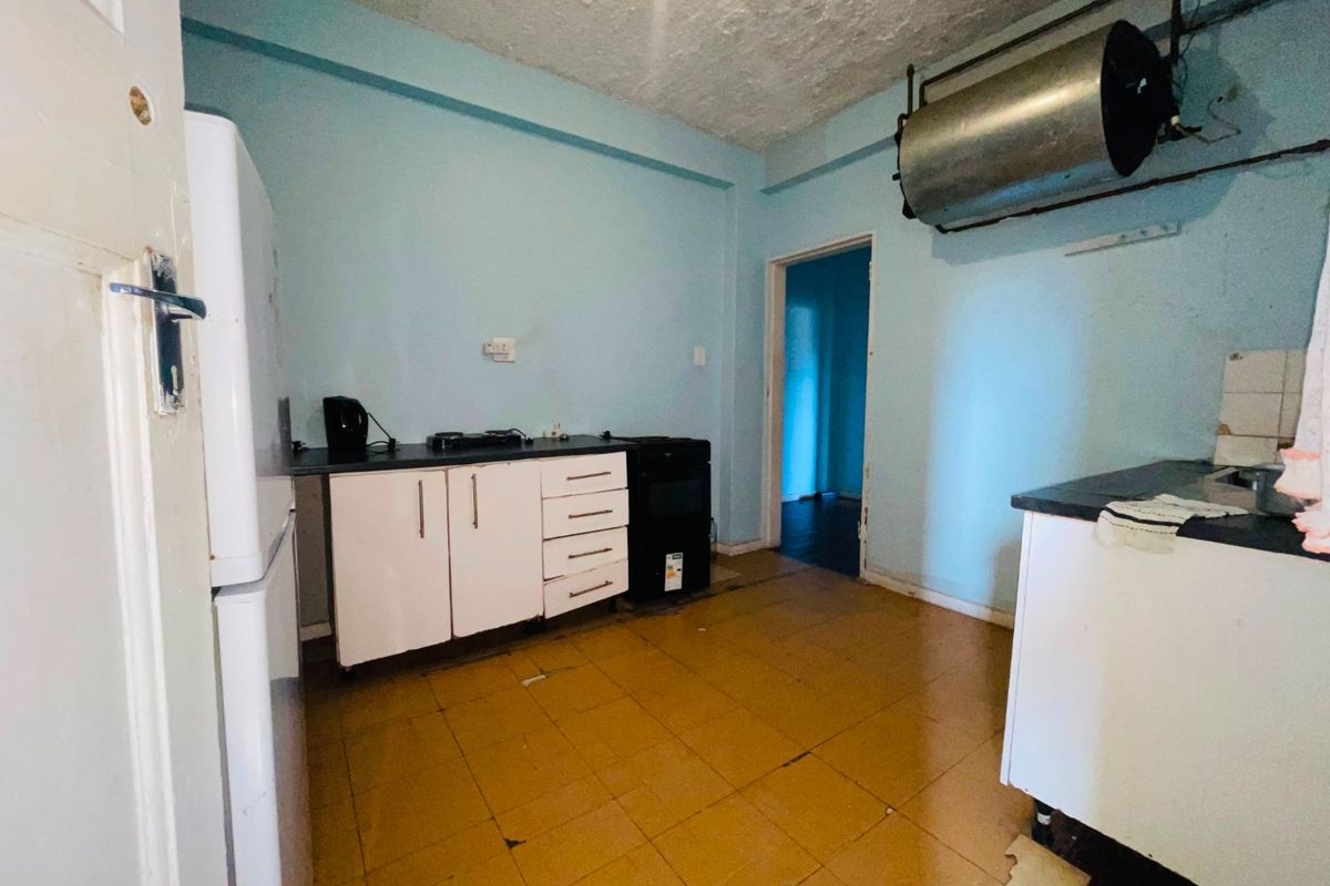 A dated kitchen featuring basic cabinetry, laminate countertops, and an exposed water heater cylinder, requiring significant renovation and modernization.