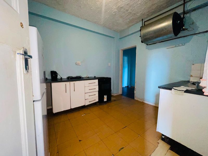 A dated kitchen featuring basic cabinetry, laminate countertops, and an exposed water heater cylinder, requiring significant renovation and modernization.