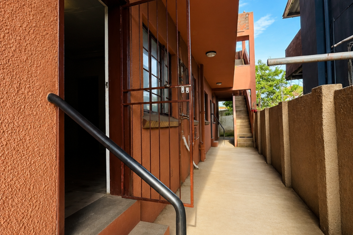 Exterior rear walkway of the apartment building featuring concrete stairs, security gates, and a boundary wall.