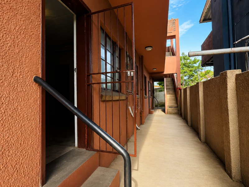 Exterior rear walkway of the apartment building featuring concrete stairs, security gates, and a boundary wall.