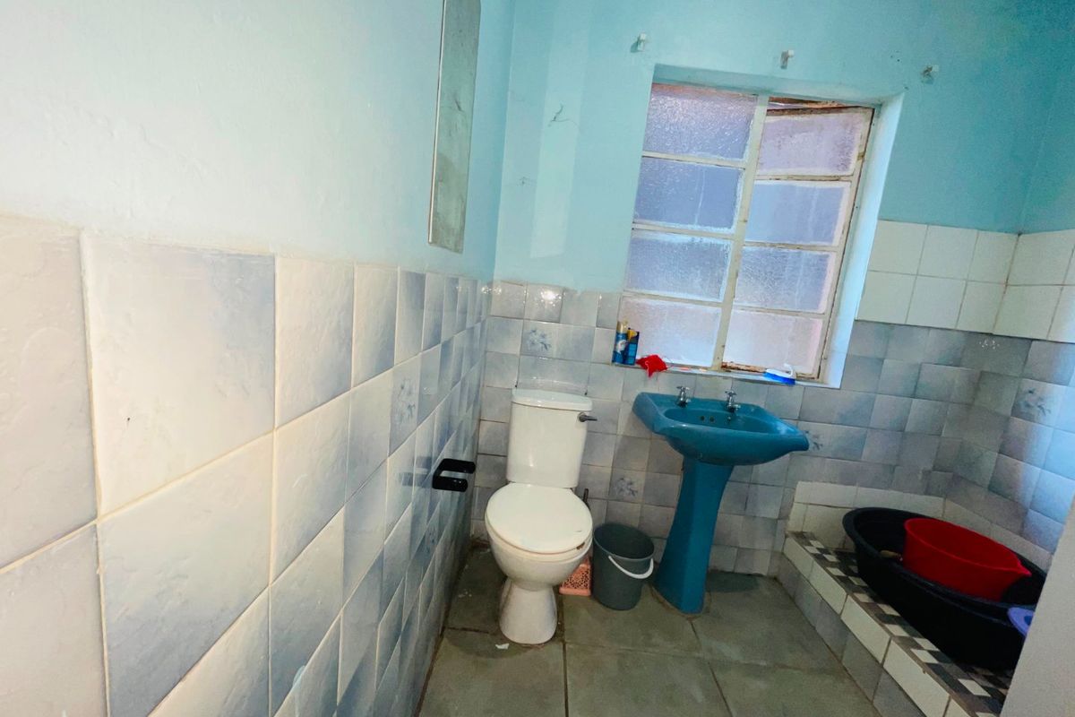 A dated bathroom featuring a pedestal basin, toilet, and tiled finishes, requiring cosmetic updates to modernize the space.