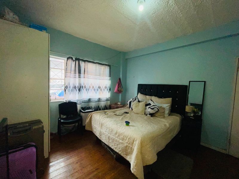 A bedroom featuring timber flooring and a window with security bars, requiring cosmetic updates to improve the overall finish and appeal.