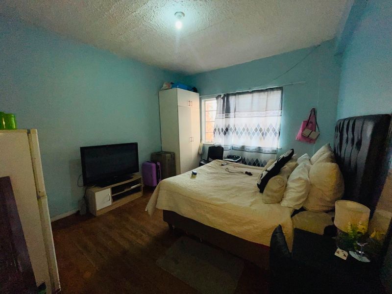 A bedroom featuring laminate flooring, a built-in wardrobe, and textured ceiling, currently requiring cosmetic updates to improve the overall finish and appeal.