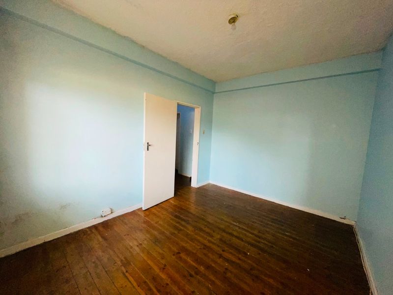 An empty bedroom featuring original hardwood flooring and light blue painted walls, requiring cosmetic updates and refurbishment.