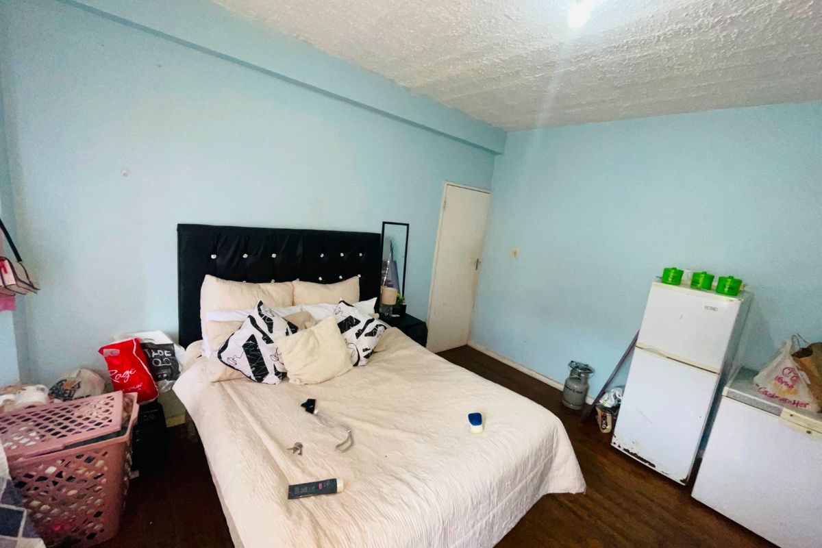 A bedroom featuring timber flooring and textured ceilings, currently requiring cosmetic updates to the wall finishes and general maintenance.