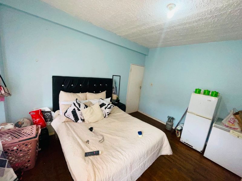 A bedroom featuring timber flooring and textured ceilings, currently requiring cosmetic updates to the wall finishes and general maintenance.