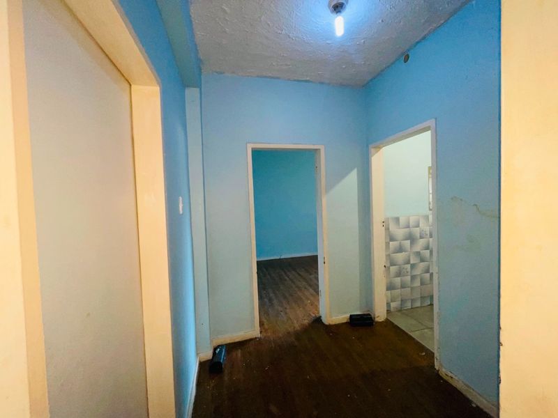 A vacant hallway featuring laminate flooring and blue painted walls with visible surface wear and damage, leading into adjacent rooms.