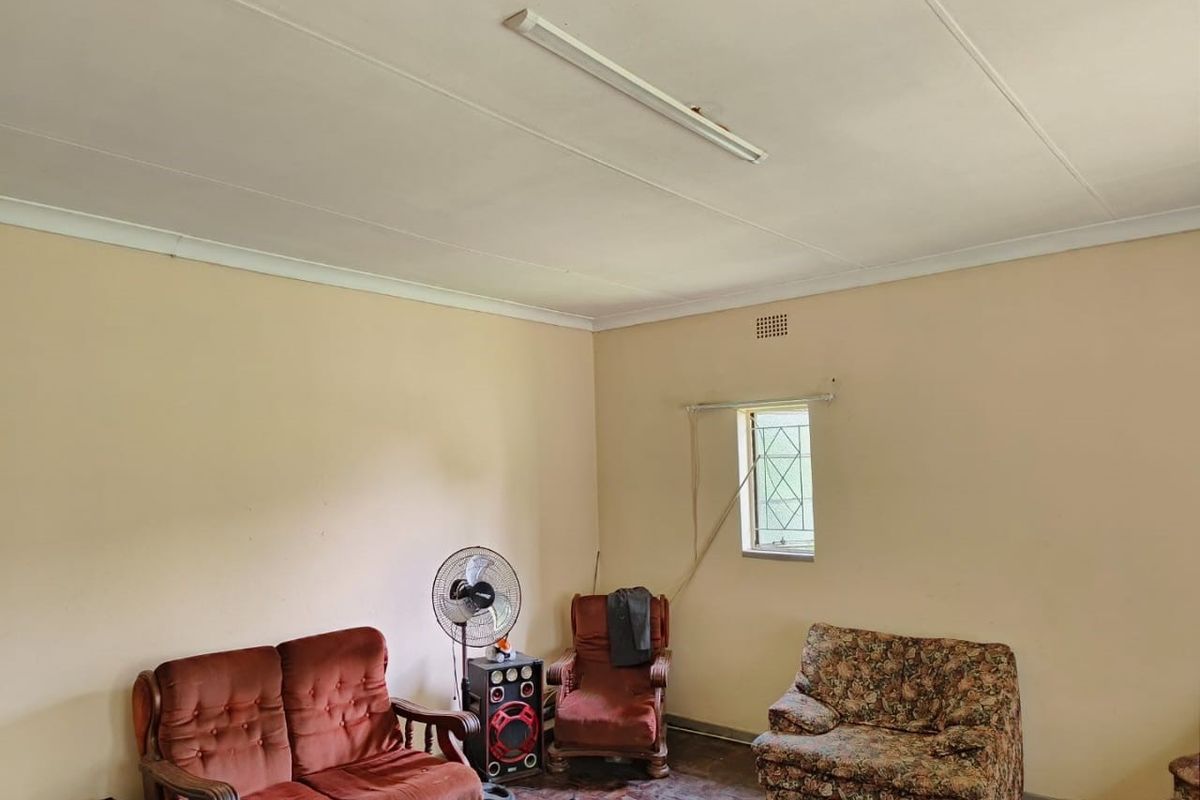 A living room featuring parquet flooring, a fluorescent ceiling light, and a window with a security gate.