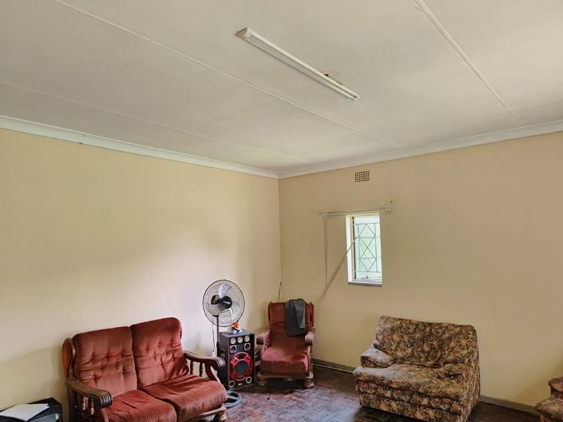 A living room featuring parquet flooring, a fluorescent ceiling light, and a window with a security gate.