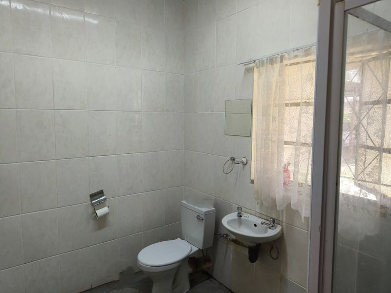 A functional bathroom featuring full-height ceramic wall tiling, a wall-mounted basin, and a standard toilet, with a window providing natural light.