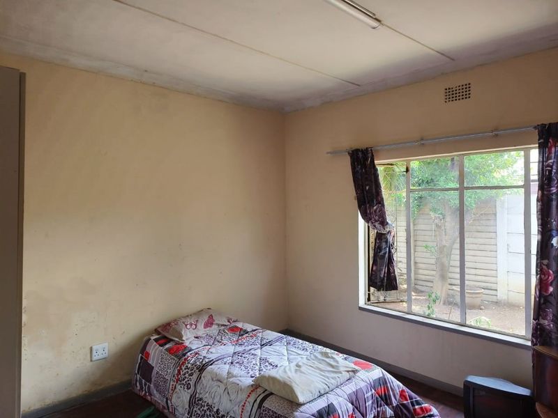 A bedroom featuring a steel-framed window, ventilation grille, and neutral wall finishes, requiring cosmetic updates to improve its overall condition.