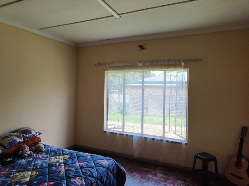A bedroom featuring parquet flooring, security bars on the window, and a ceiling vent. The room requires cosmetic updates to improve its overall condition.