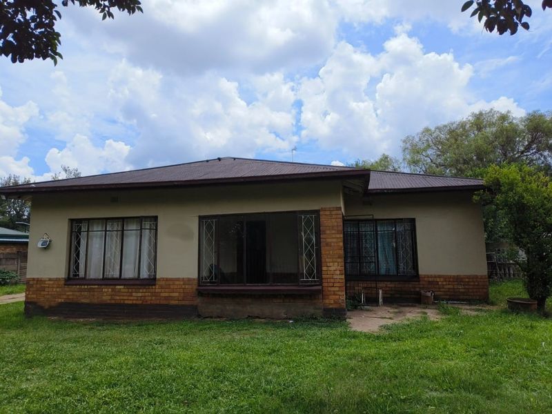 Front elevation of a single-story house featuring a corrugated metal roof, brick base, and steel-framed windows with security bars.