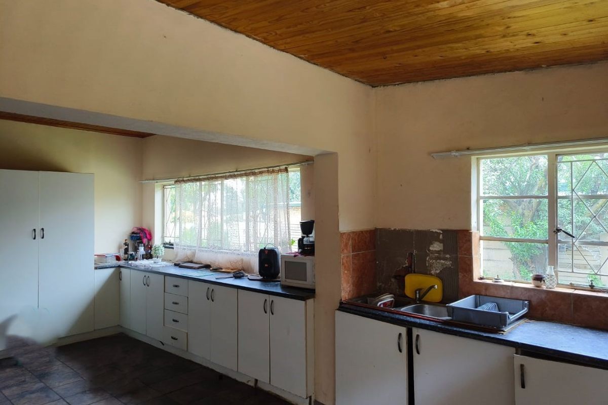 A dated kitchen featuring built-in cabinetry, laminate countertops, a double sink, and a timber ceiling, offering significant potential for modernization and renovation.