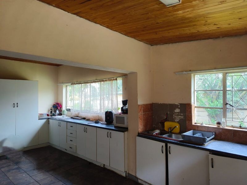 A dated kitchen featuring built-in cabinetry, laminate countertops, a double sink, and a timber ceiling, offering significant potential for modernization and renovation.