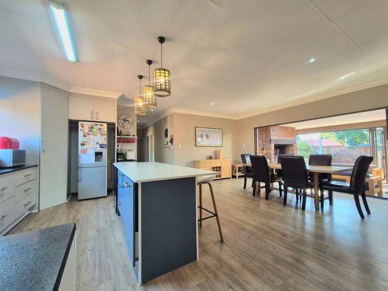 Spacious open-plan kitchen and dining area featuring a central island, modern cabinetry, laminate flooring, and seamless flow to an outdoor patio with a brick fireplace.