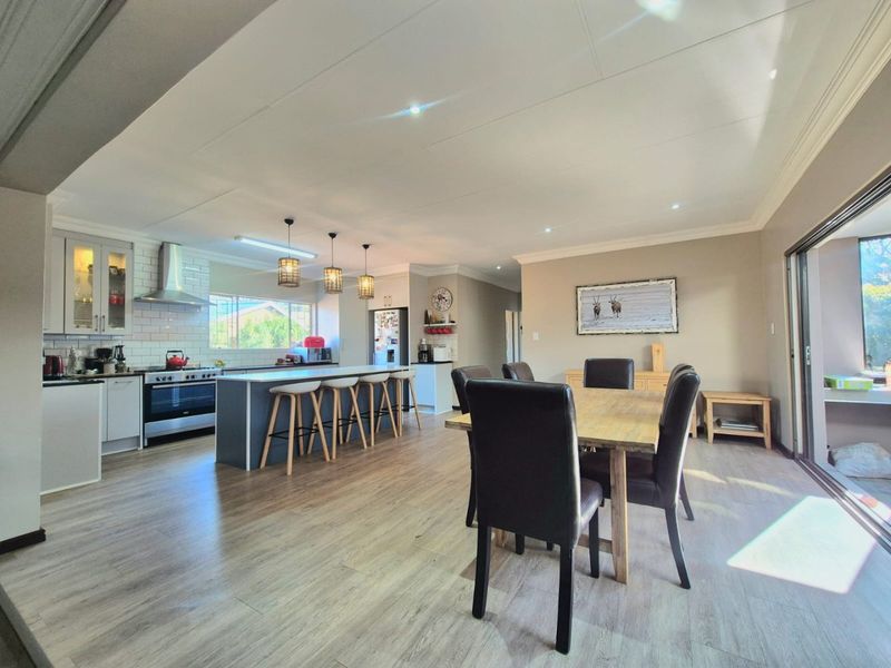 Spacious open-plan kitchen and dining area featuring a large central island, modern cabinetry, subway tile backsplash, and seamless access to the outdoor patio.